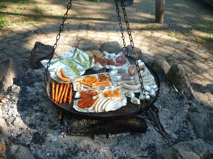 Feuerstelle im Garten mit Schwenkgrill mit Grillfleisch und Würstchen
